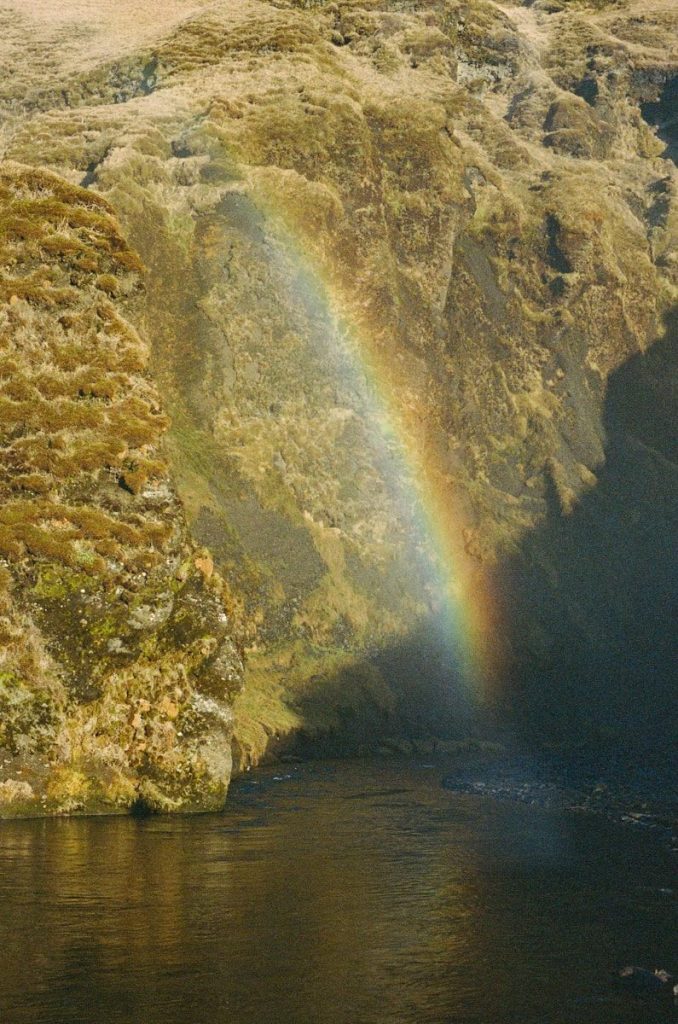 Rainbow arches across a rugged cliff above a dark river.
